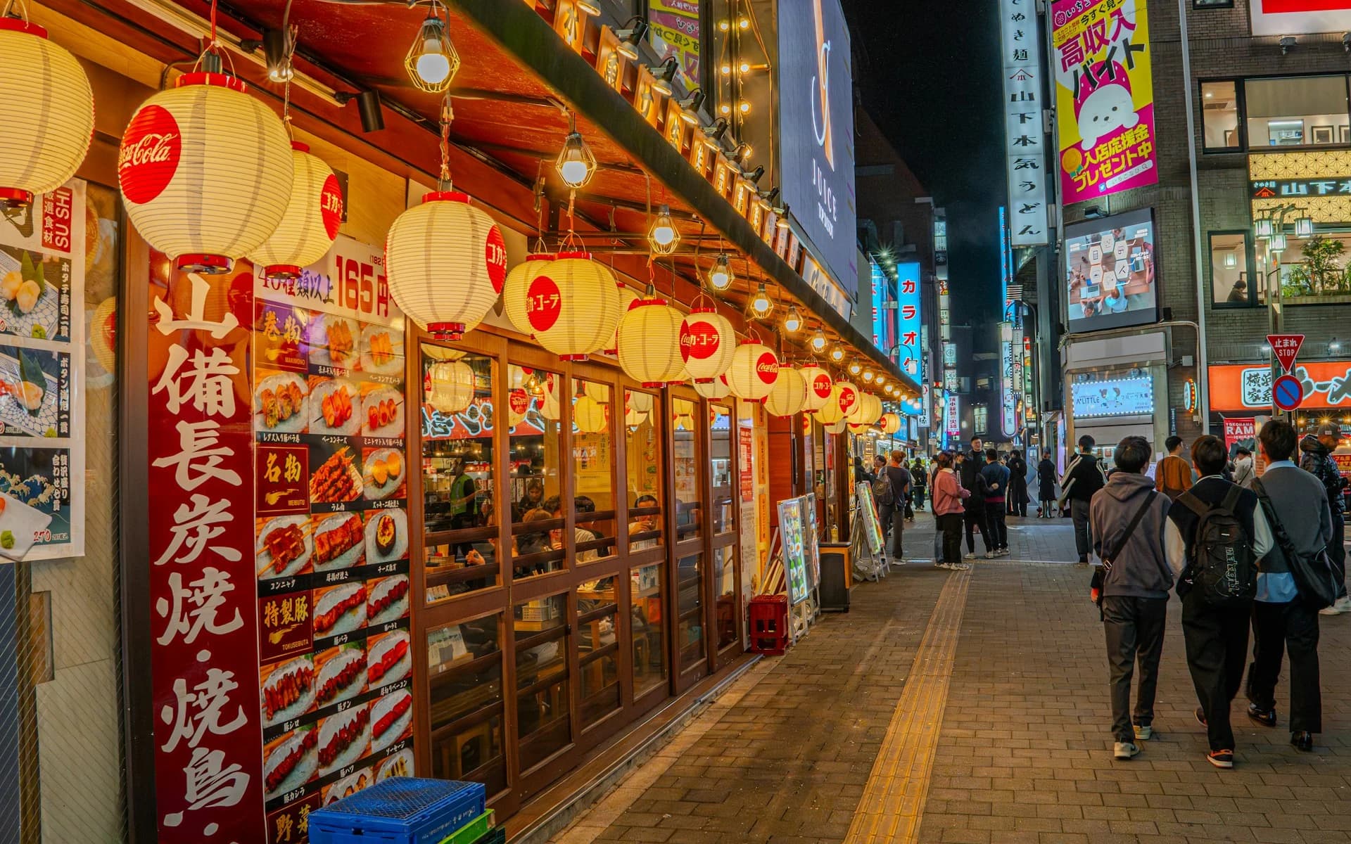 Neon-lit backstreet izakaya alley behind Shibuya crossing filled with evening diners